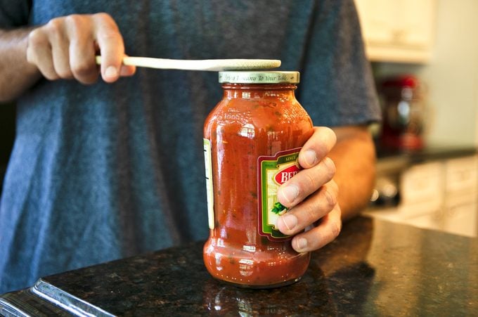 man tapping the lid of a jar with a wooden spoon
