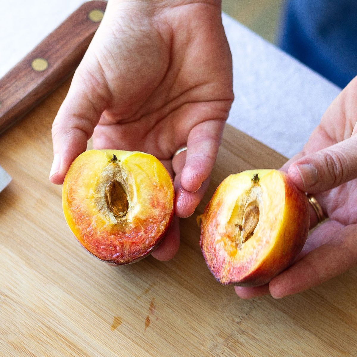 Two hands holding two halves of a fresh peach.