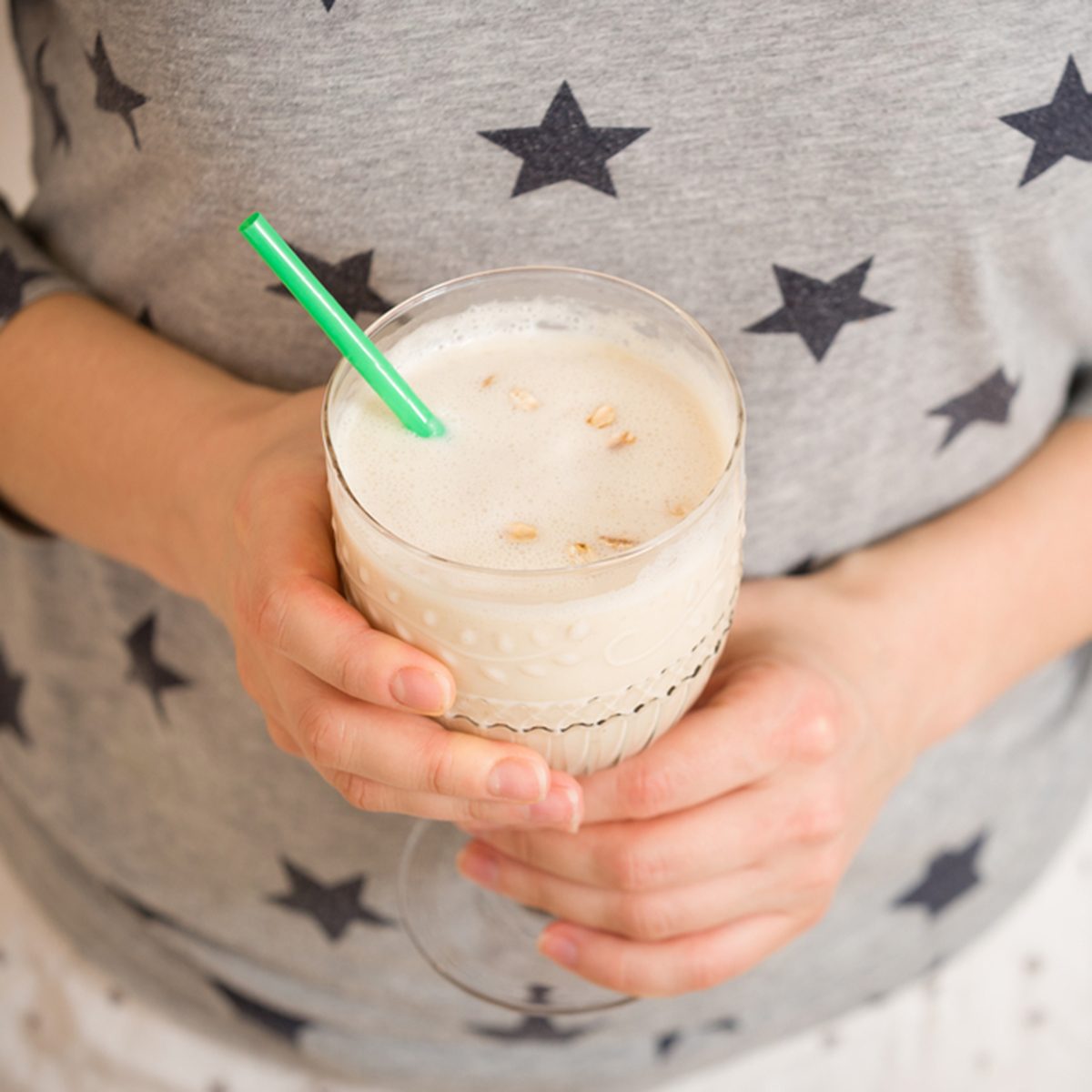 Young woman with a big glass of healthy smoothie served with a straw and oats. Hands holding milkshake. Stars background. Dairy snack or breakfast.; Shutterstock ID 540214360