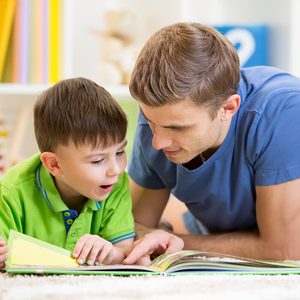 kid boy and his father read a book on floor at home