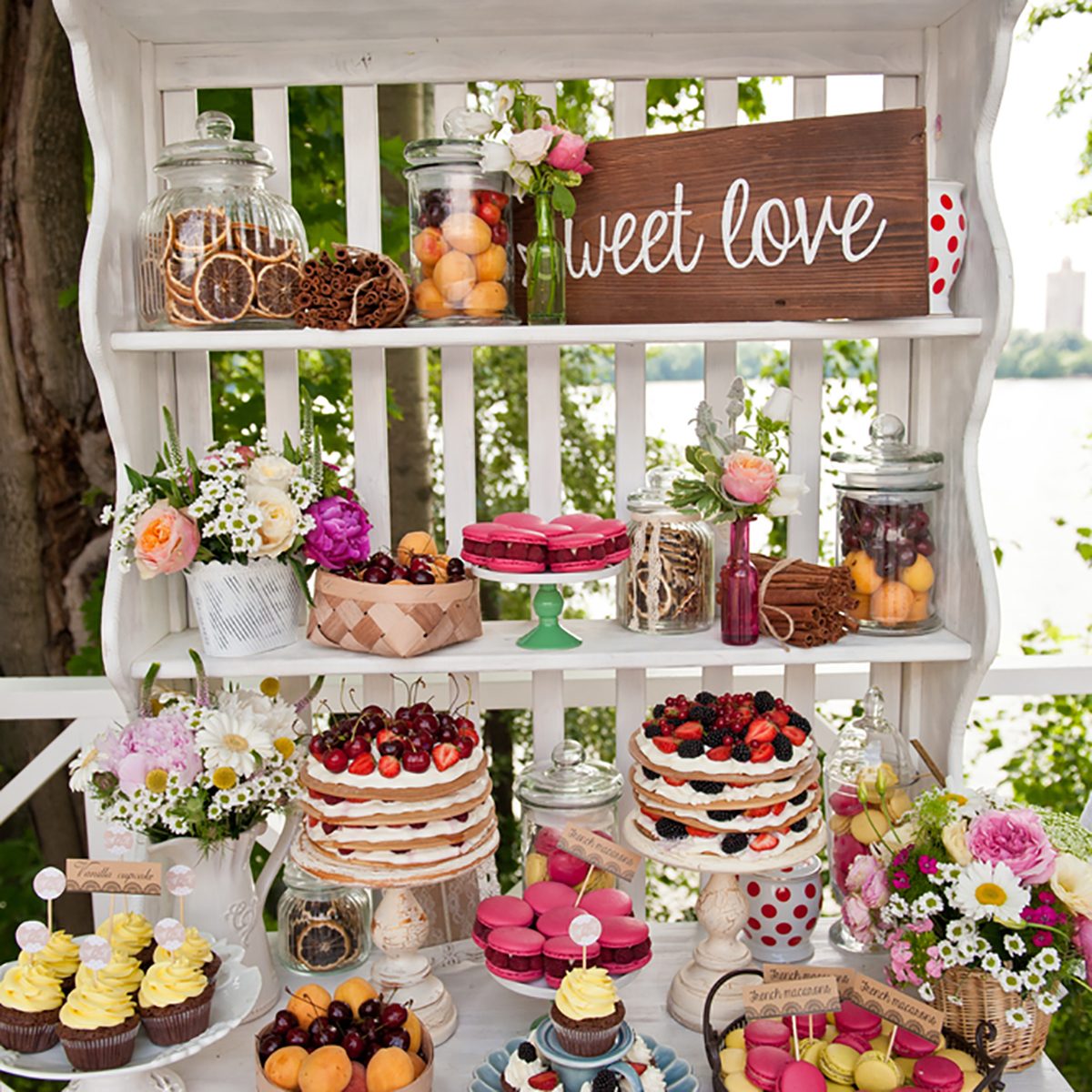 Sweet bar on summer wedding. Layer cakes with protein cream and fresh cherry and berries on a cake stand outdoors