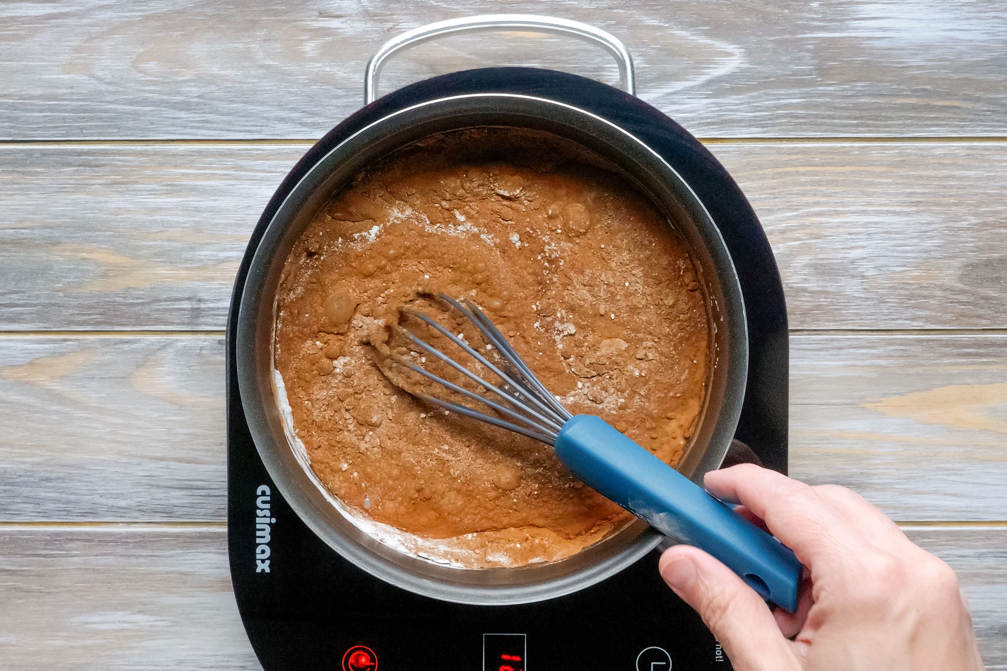 Whisking Sugar, Cocoa, Cornstarch and Salt in a Saucepan on Induction Stove on Wooden Surface
