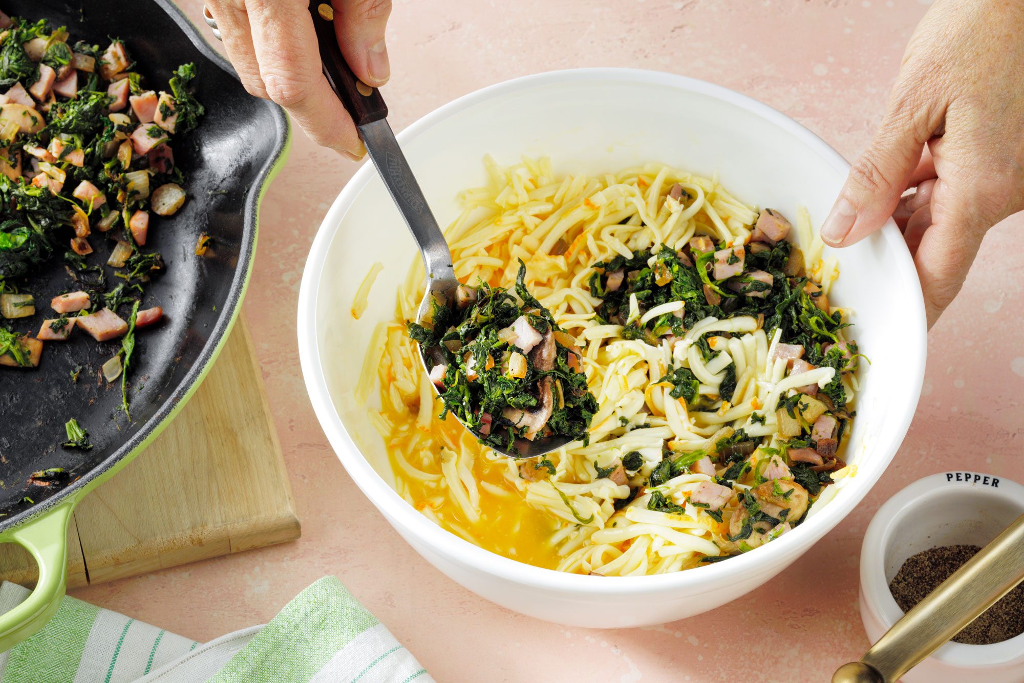 a person mixing spinach, ham, cheese and beaten egg in a large white bowl