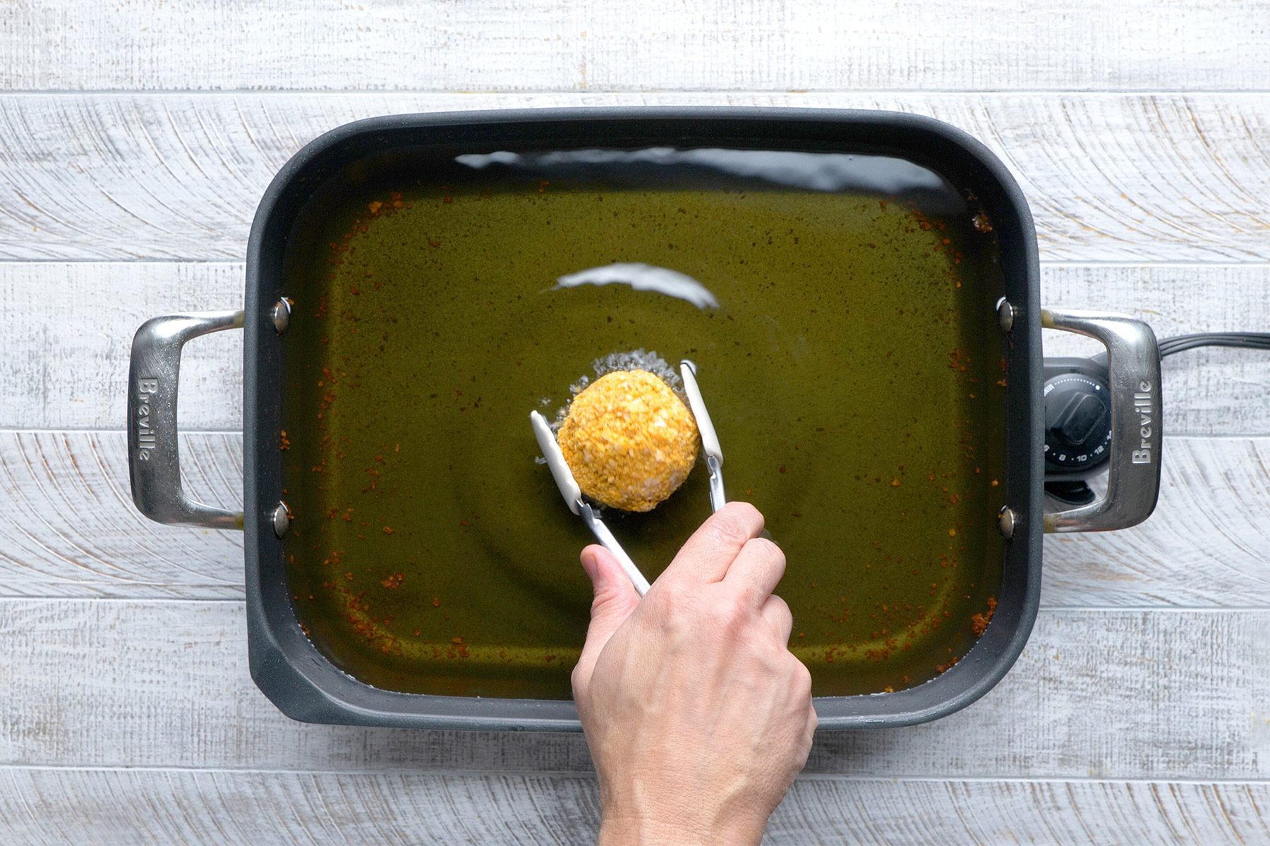 overhead shot; white wooden background; In an electric skillet or deep-fat fryer, Frying ice cream ball until golden