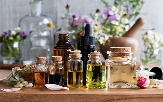 Selection of essential oils, with herbs and flowers in the background