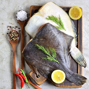 Raw fish flatfish on a wooden board with lemon and spices gray background. copy Space