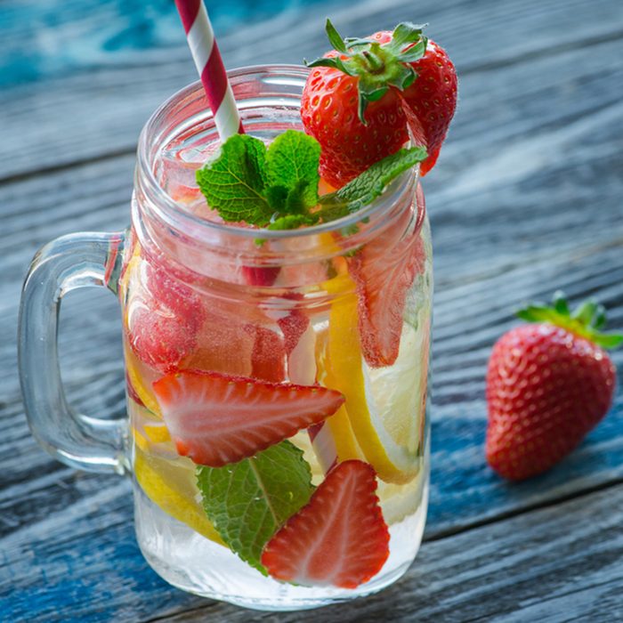 Jug with lemon and strawberry infused water on a rustic wooden table