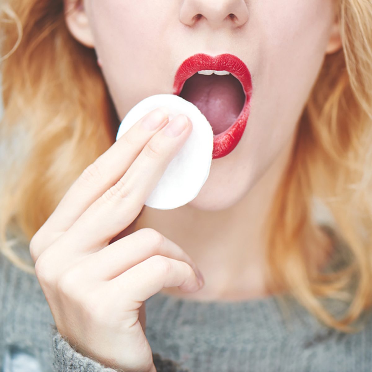 A young girl wipes the red lipstick, close-up;