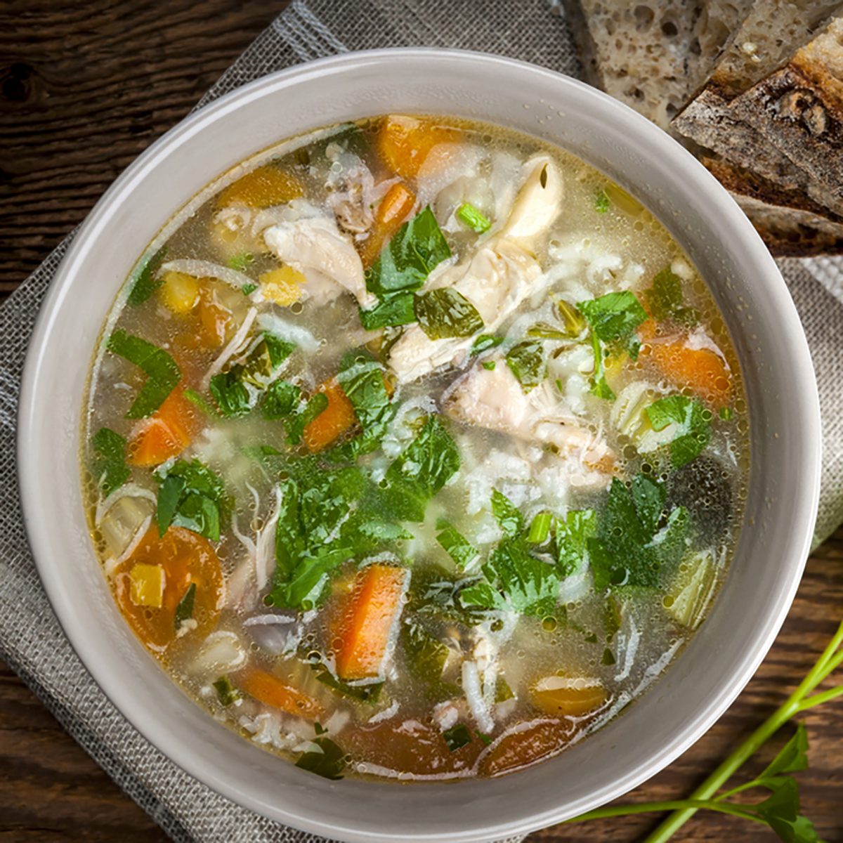 Chicken rice soup with vegetables in bowl and bread from above