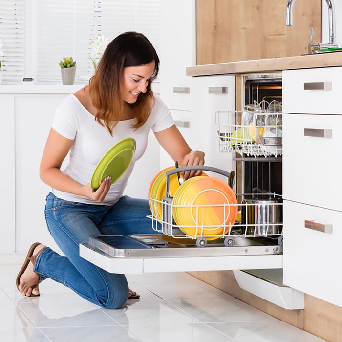 Happy Young Woman Arranging Plates In Dishwasher At Home