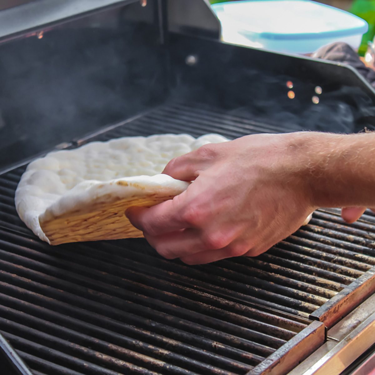 Hand flipping flatbread cooking on outside electric grill showing browned bottom and top not yet cooked
