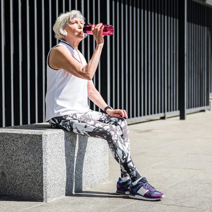 Tired senior lady having rest after exercise beside metal fence