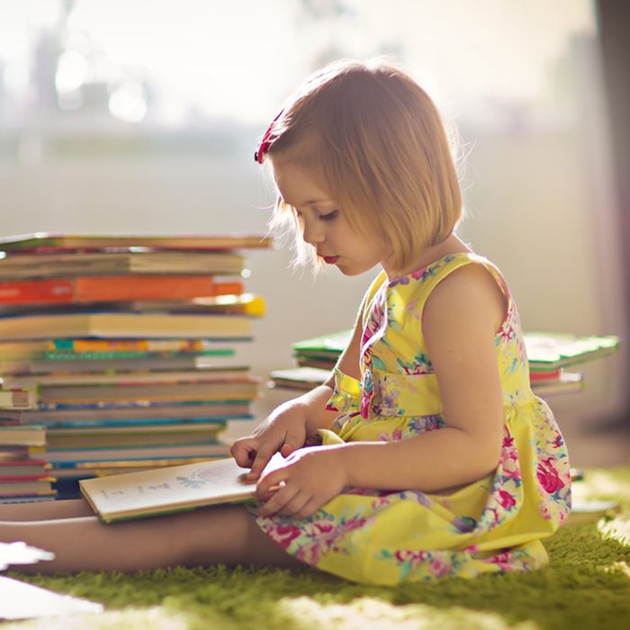 A little cute girl in a yellow dress reading a book sitting on the floor