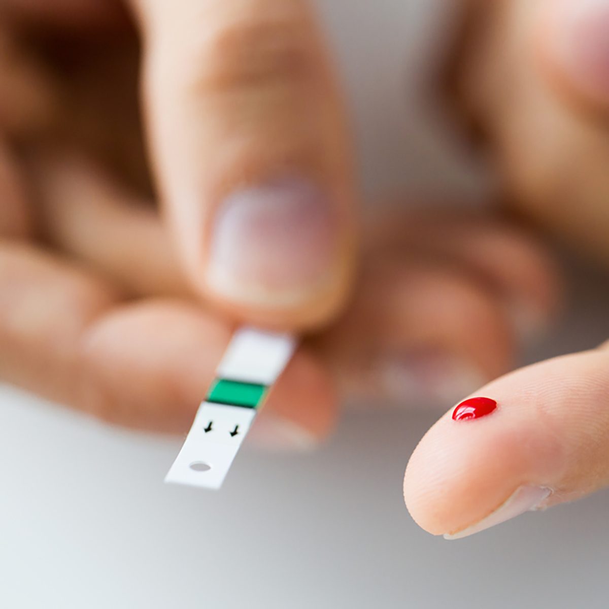 medicine, diabetes, glycemia, health care and people concept - close up of male finger with blood drop and test stripe;