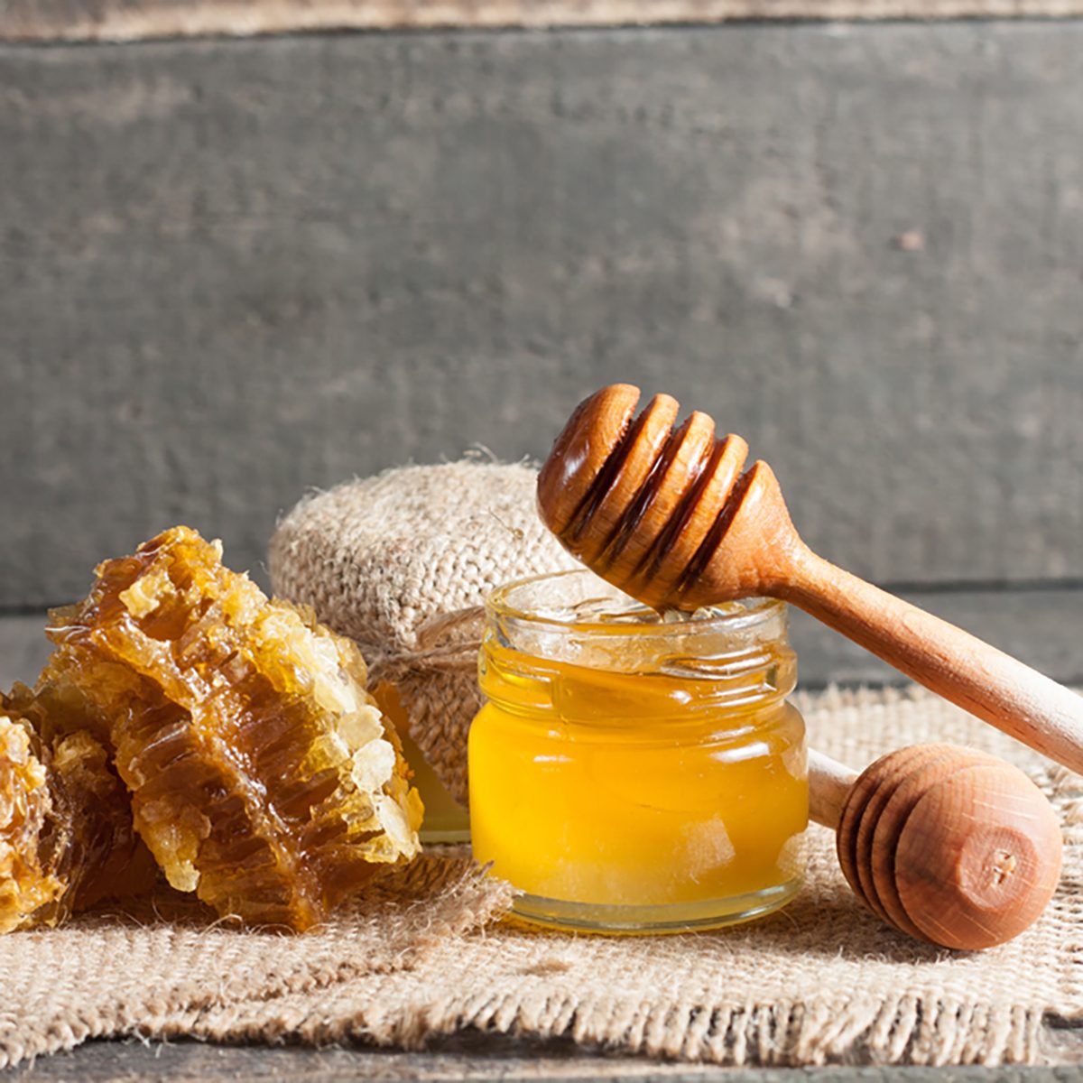 Honey dripping from a wooden honey dipper in a jar on wooden grey rustic background