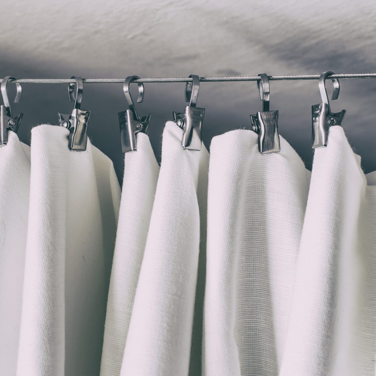 cream-colored curtain hanging on a string on a metal hook in white ceiling illuminated by daylight