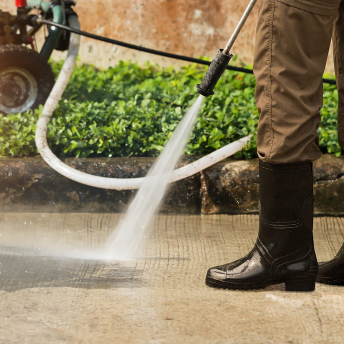 Worker cleaning driveway with gasoline high pressure washer splashing the dirt