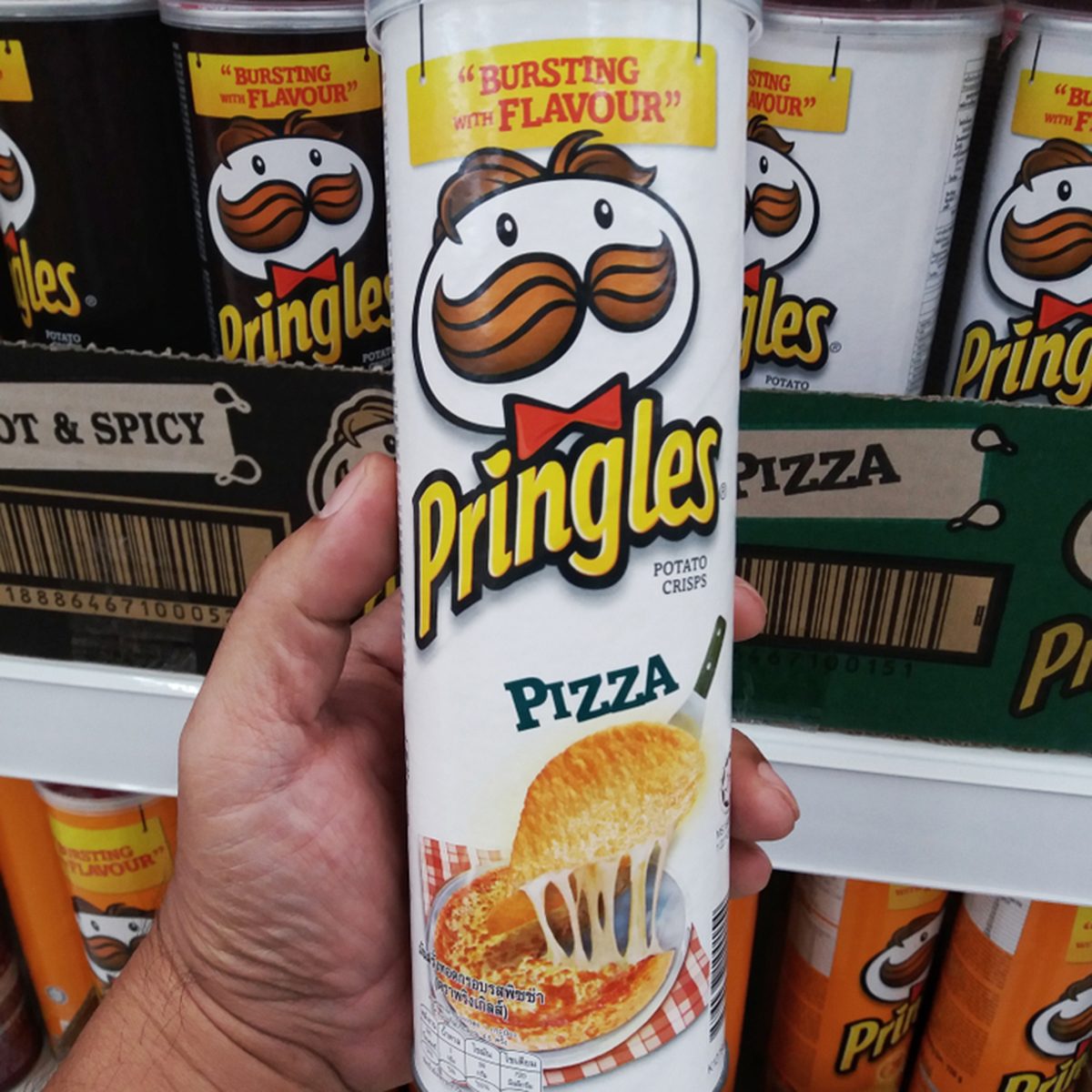 Hand holding a tube of pizza flavour Pringles potato chips. Pringles is an American brand of snack chips owned by Kellogg