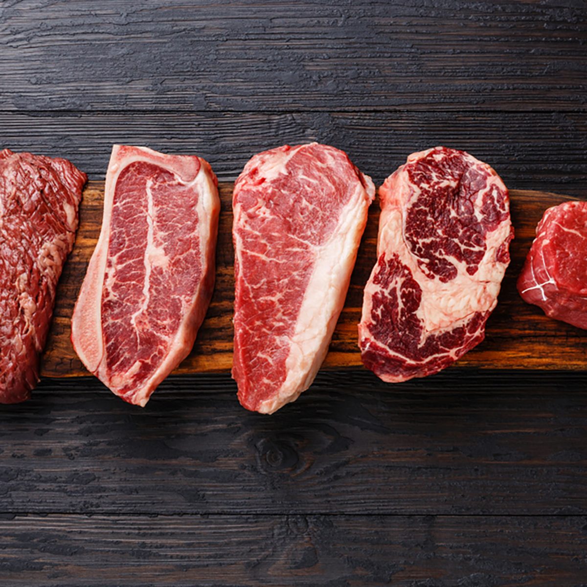 Variety of Raw Black Angus Prime meat steaks Machete, Blade on bone, Striploin, Rib eye, Tenderloin fillet mignon on wooden board