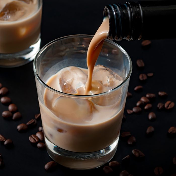 Pouring irish cream in a glass with ice, surrounded by coffee beans on a dark black background