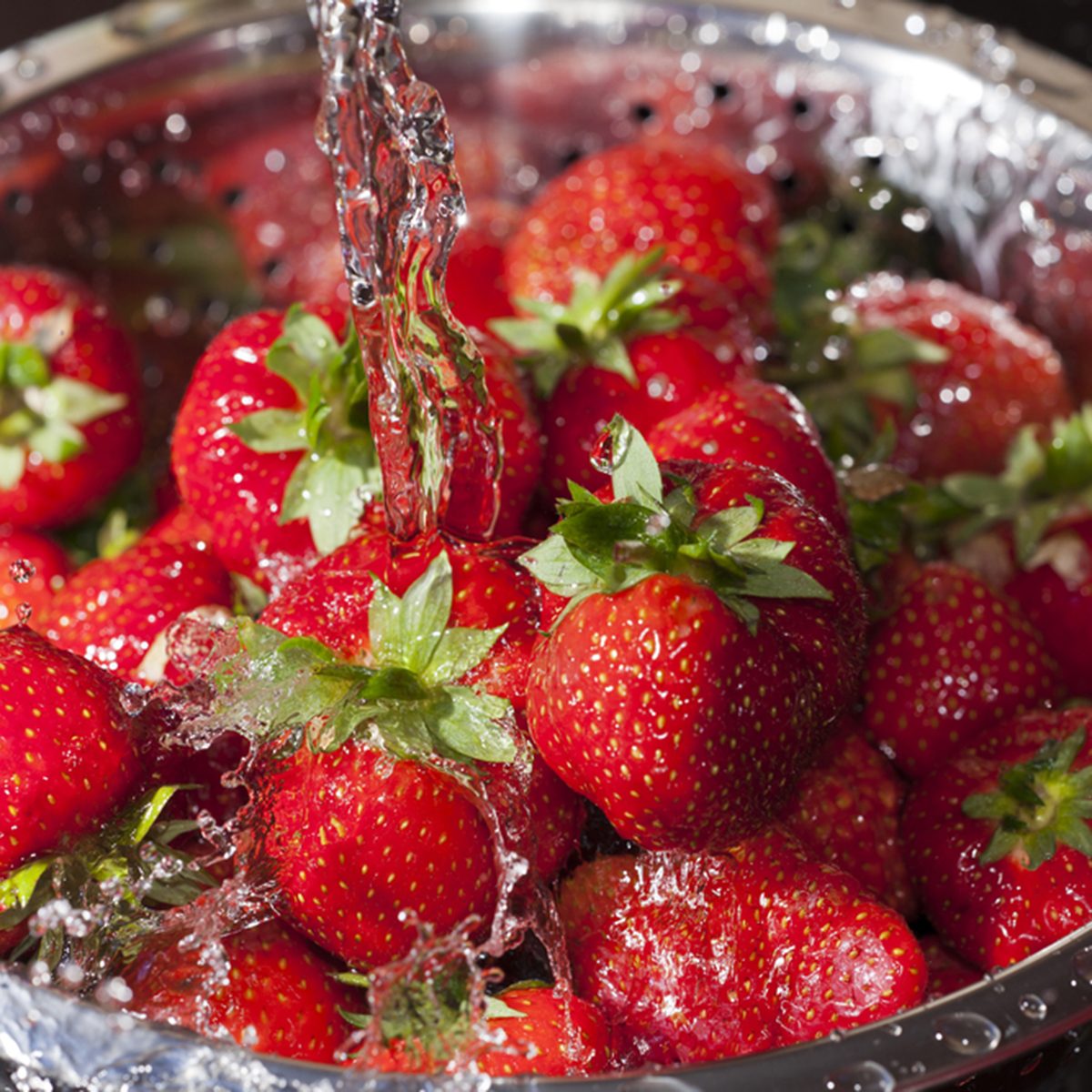 Red ripe strawberries in a stainless steel colander are rinsed under water