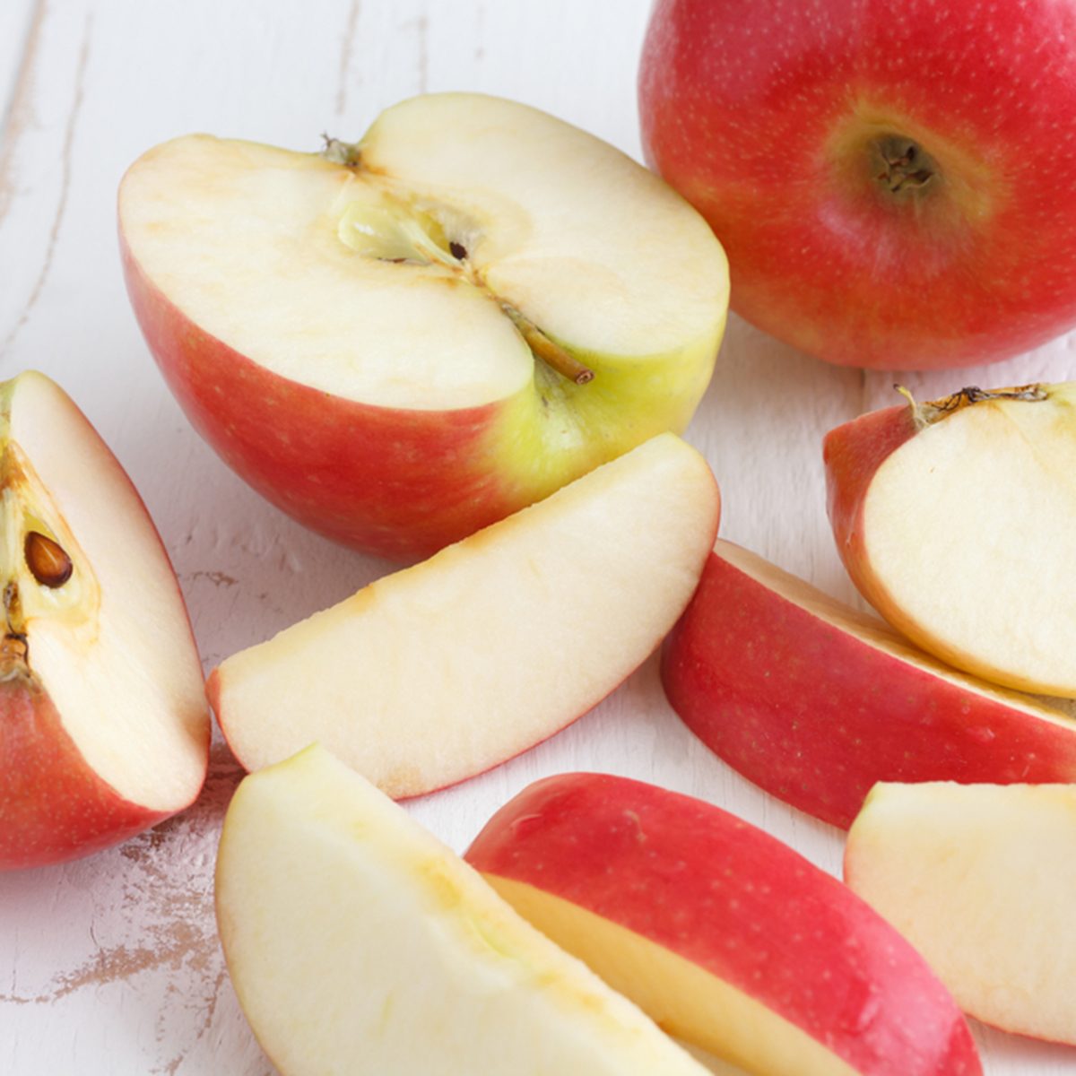 Pink lady apples cut on a painted white rustic wood table.