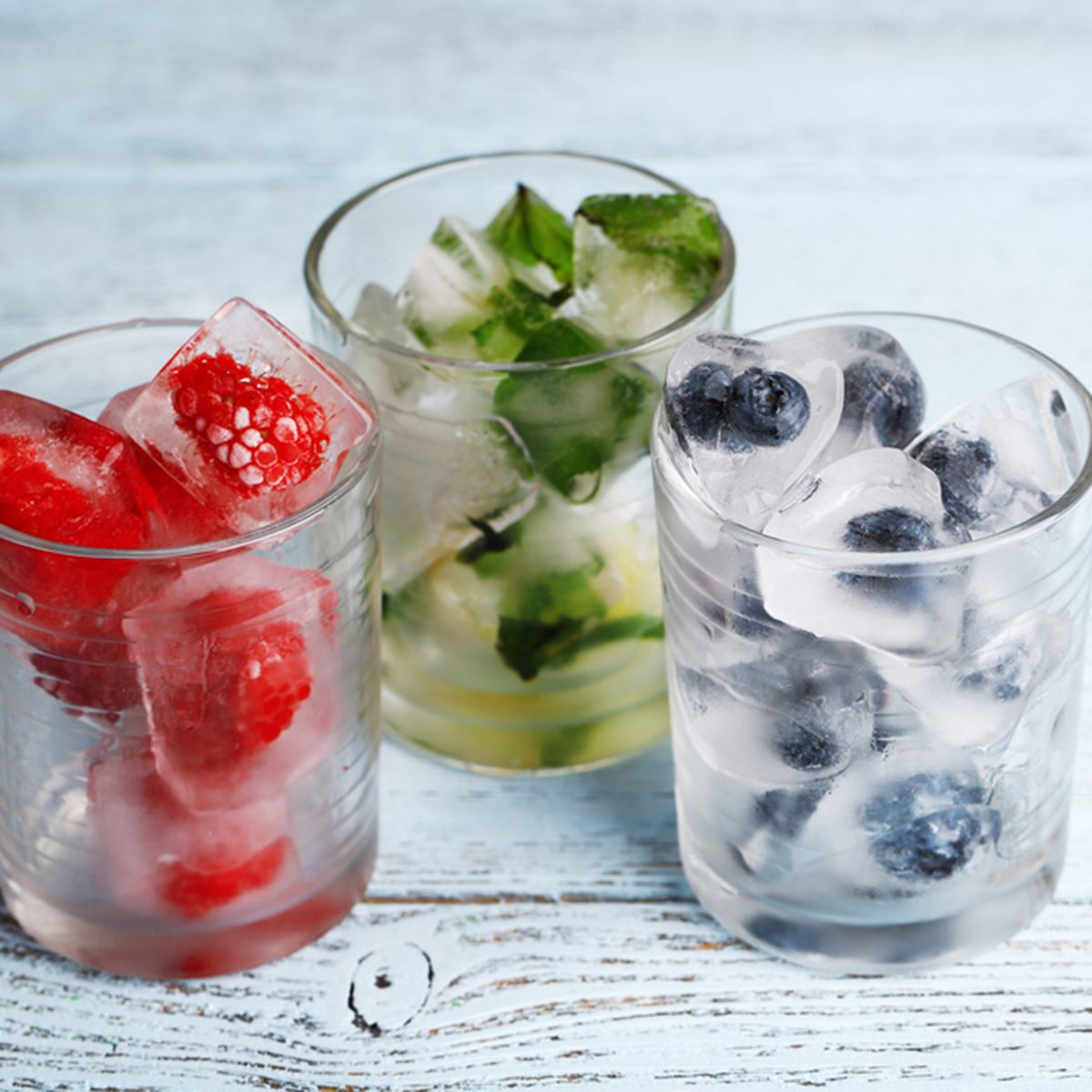 Ice cubes with mint leaves, raspberry and blueberry in glasses, on color wooden background