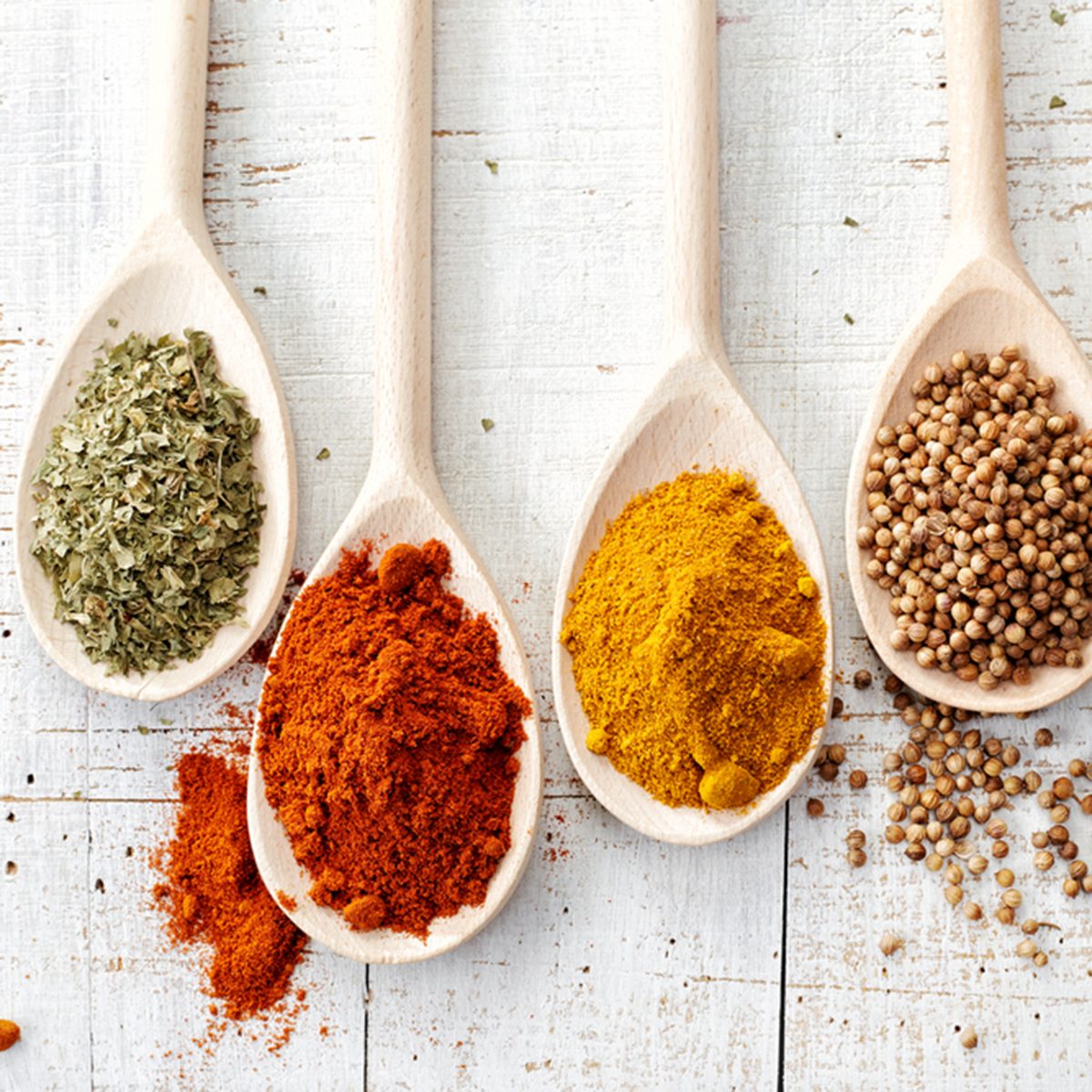 various spices in wooden spoons on old white wooden table