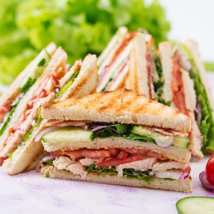 Club sandwich with chicken breast, bacon, tomato, cucumber and herbs