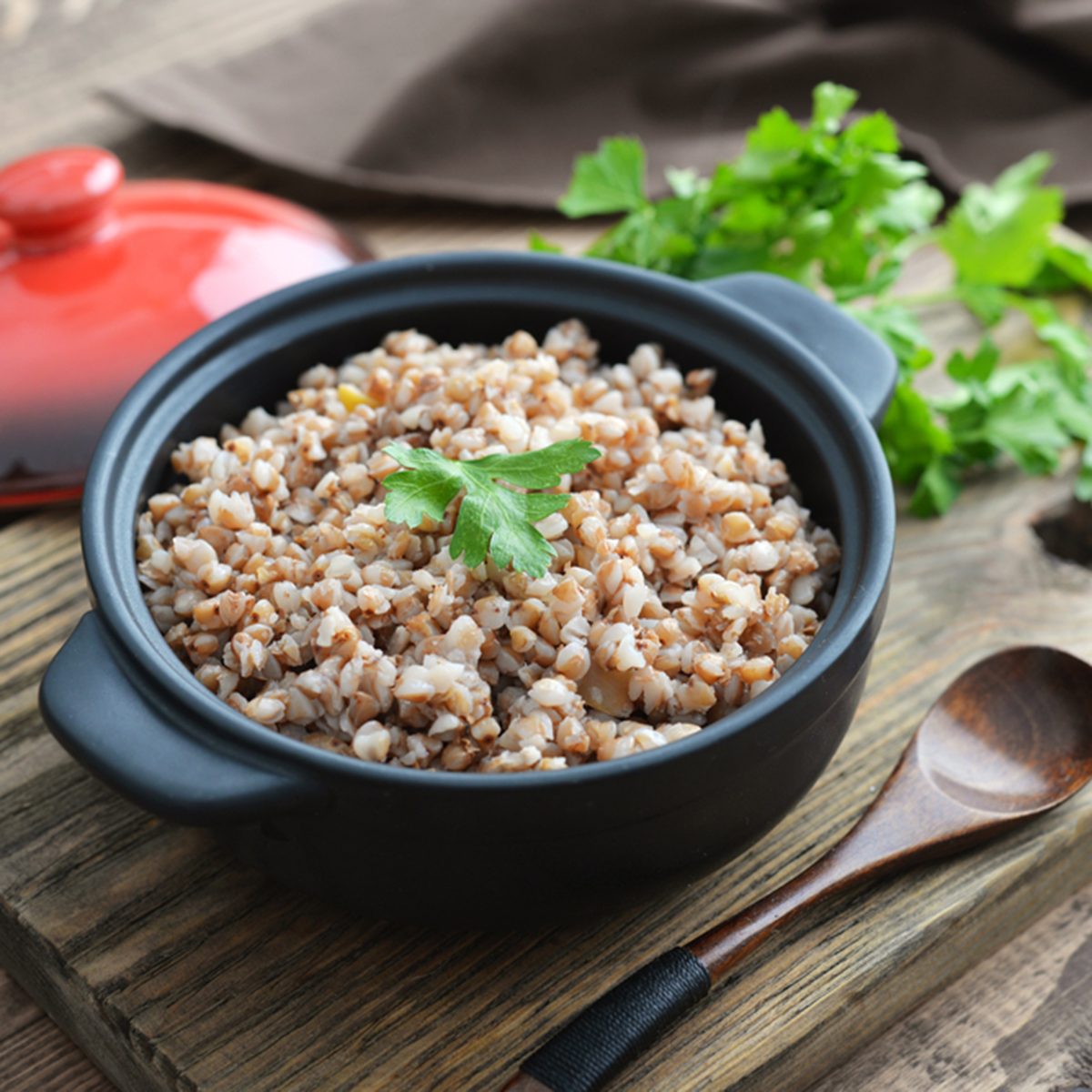 Buckwheat porridge in black casserole on wooden background closeup