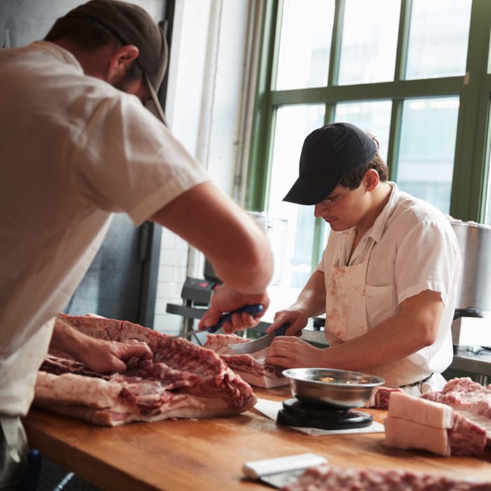 Two butchers cutting meat to sell at a butcher