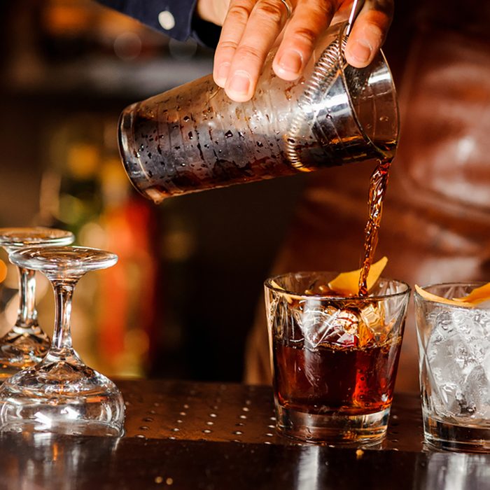 Barman pouring fresh alcoholic drink into the glasses with ice cubes on the bar counter