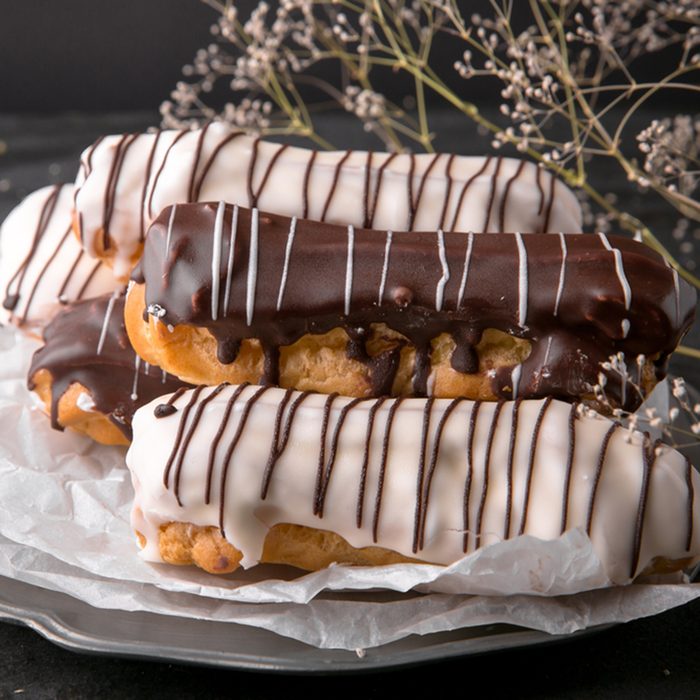 Assorted eclairs or profiteroles with black chocolate and white chocolate with custard inside on a metal plate on a dark background. Traditional French dessert. Empty space for design text template; Shutterstock ID 739322287; Job (TFH, TOH, RD, BNB, CWM, CM): Taste of Home