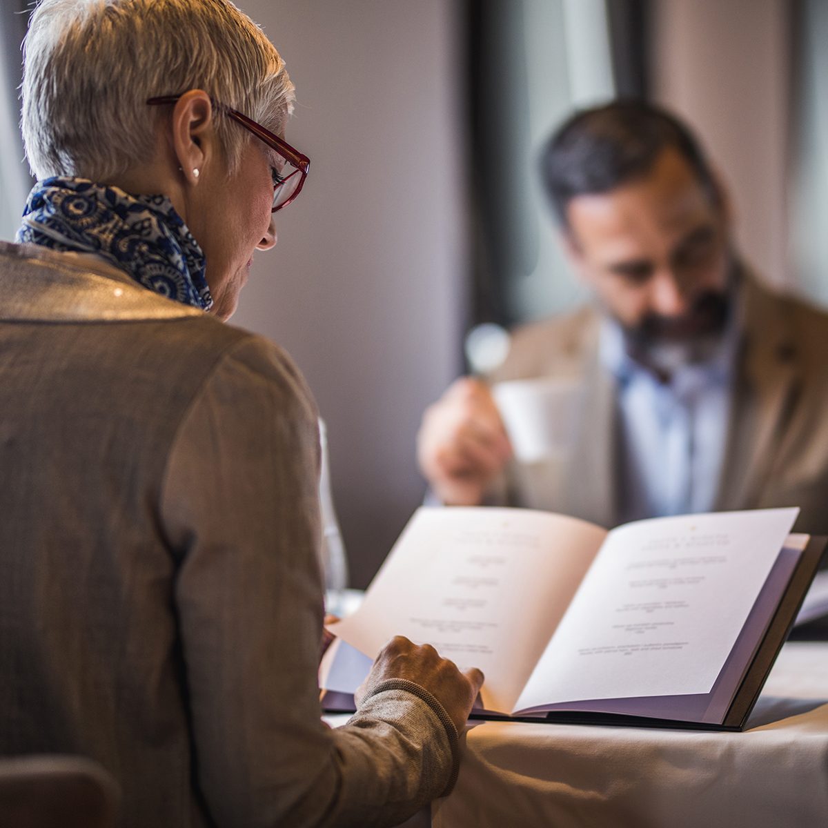 Back View Of Mature Woman Reading Menu During Lunch Time In A Restaurant.