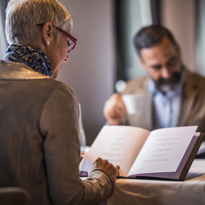 Back View Of Mature Woman Reading Menu During Lunch Time In A Restaurant.