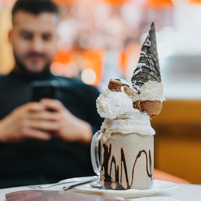 Close Up Of Dessert Served On Table With Man Using Smart Phone In Background