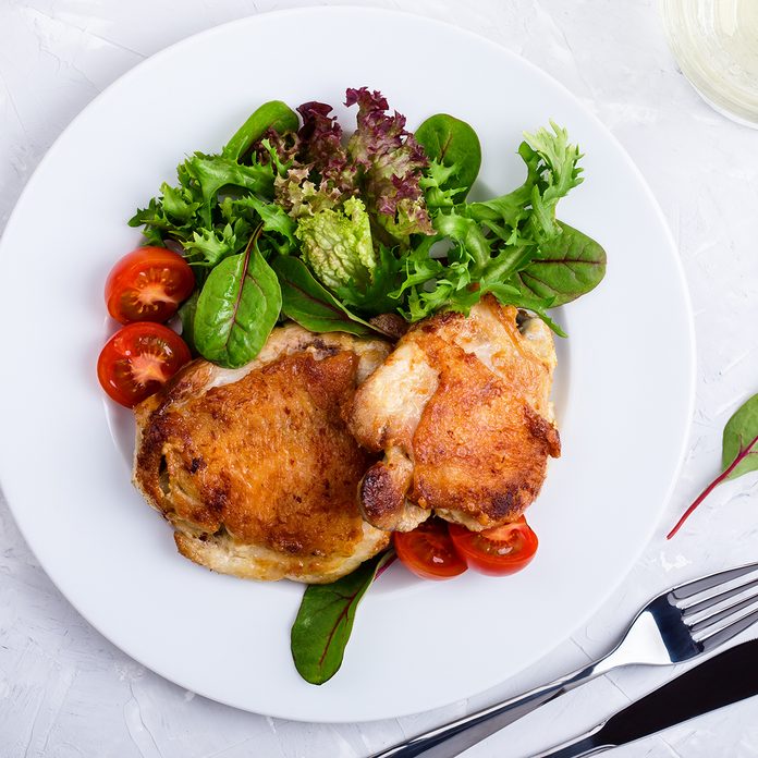 Roast Chicken Legs On White Plate Over Light Gray Plaster Texture Table