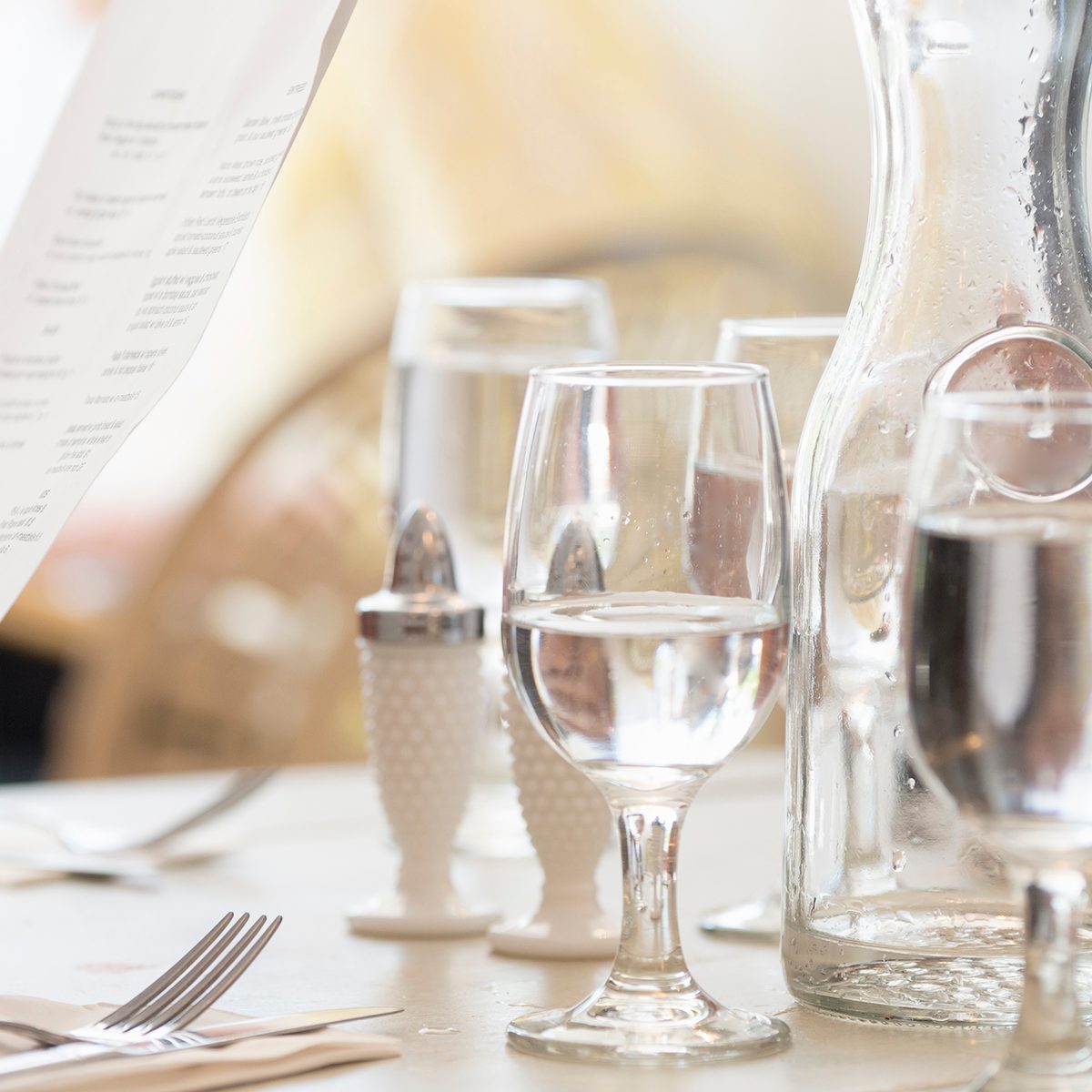 Close Up Of Wine And Water Glasses And Place Settings At A Table In A Restaurant. A Persons Hand Holding The Menu.