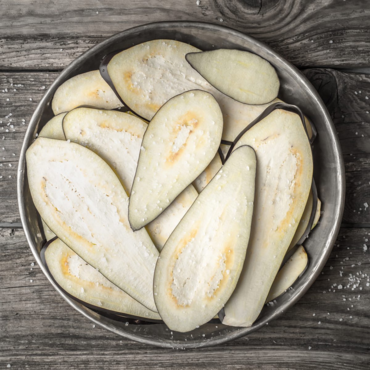 Sliced eggplants with salt in the metal plate on the wooden table top view