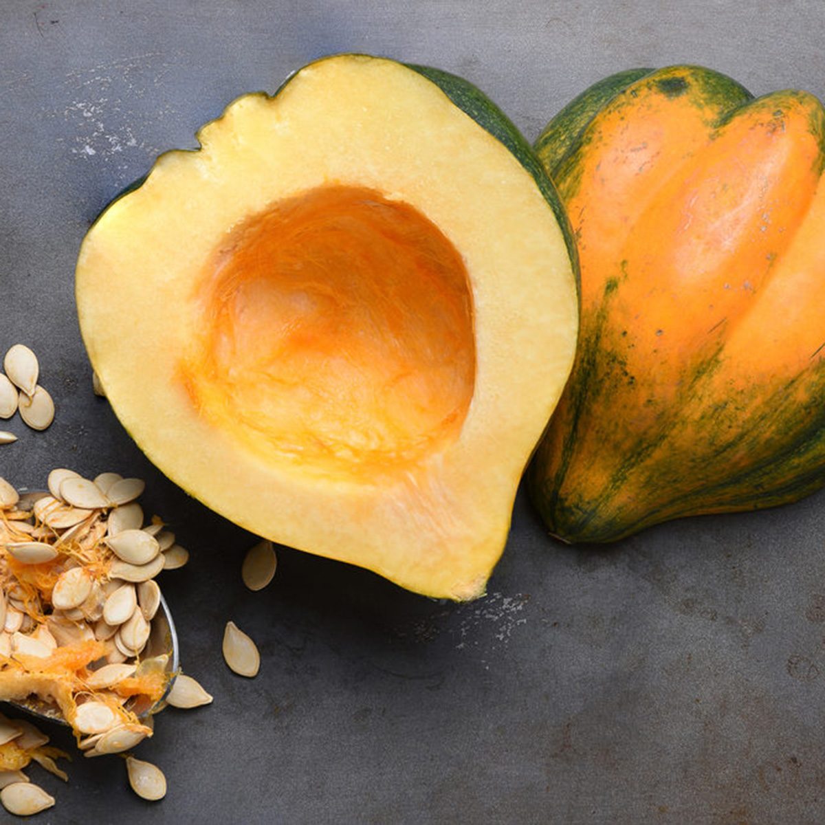 High angle view of an Acorn Squash cut in half on a metal baking sheet with a spoon and seeds scooped out.