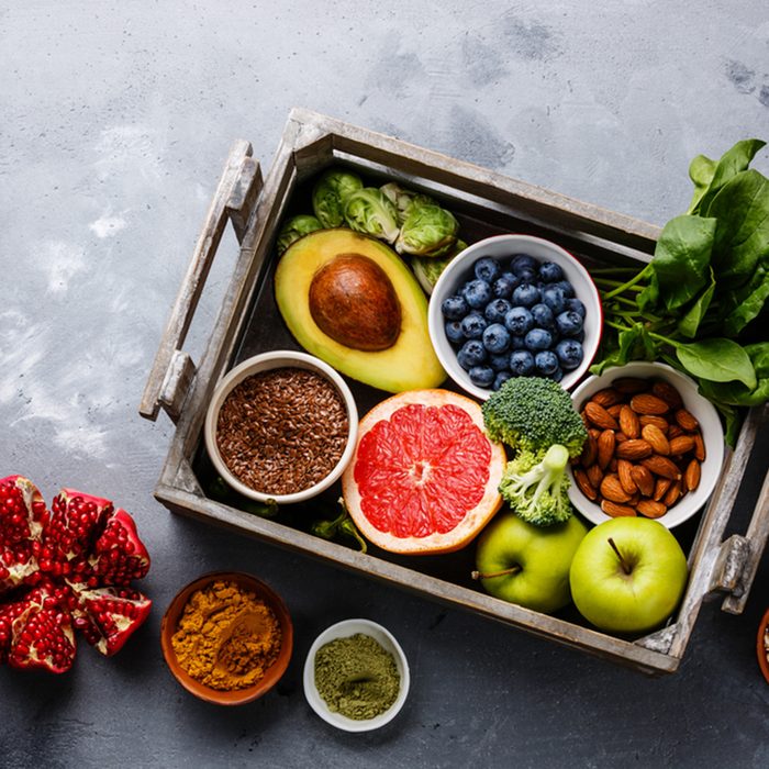 Healthy food clean eating selection in wooden box: fruit, vegetable, seeds, superfood, cereals, leaf vegetable on gray concrete background