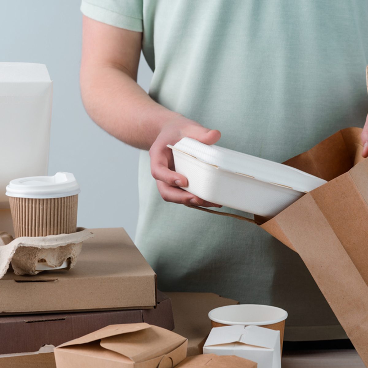 Male hands putting take-out food container into paper bag, close-up.
