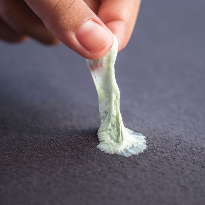 Close up hand removing sticky chewing gum from black textile or clothes