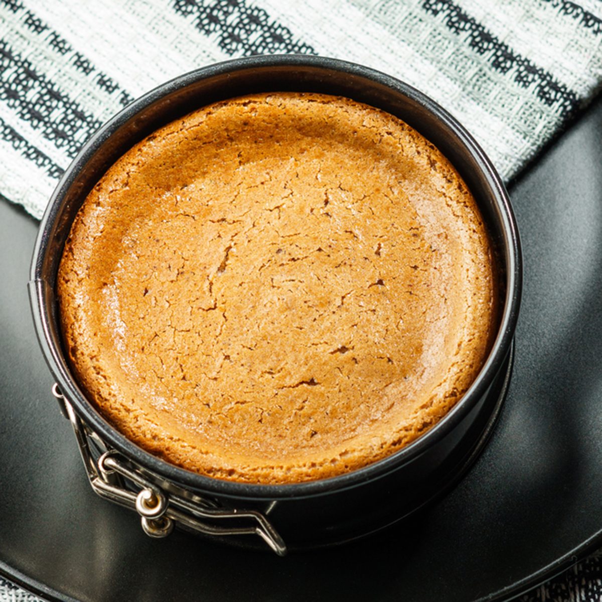 Homemade chocolate cheesecake in small springform pan on black plate on the table.