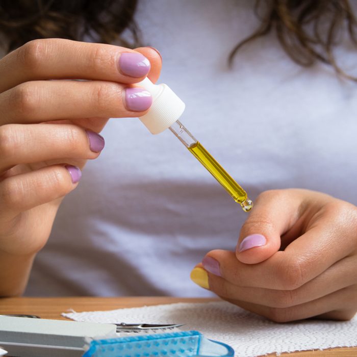 Female hands take care of cuticles with oil.