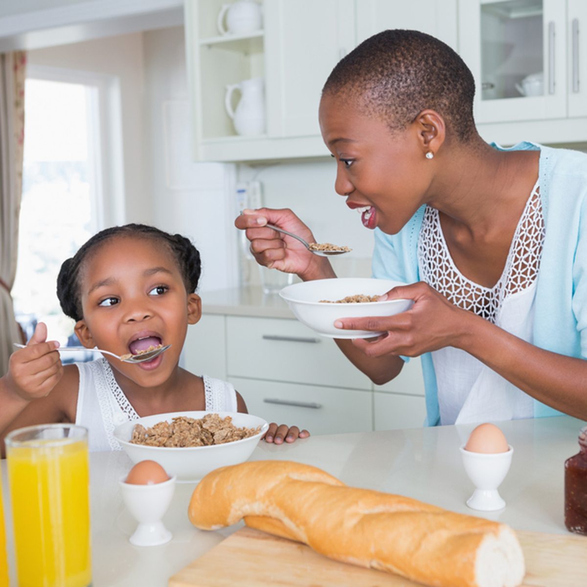 Portrait smiling mother and daughter eating together at home in the kitchen