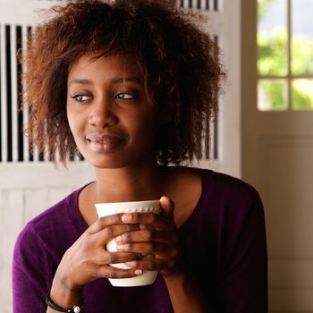 Close up portrait of a beautiful young african american woman enjoying cup of coffee at home