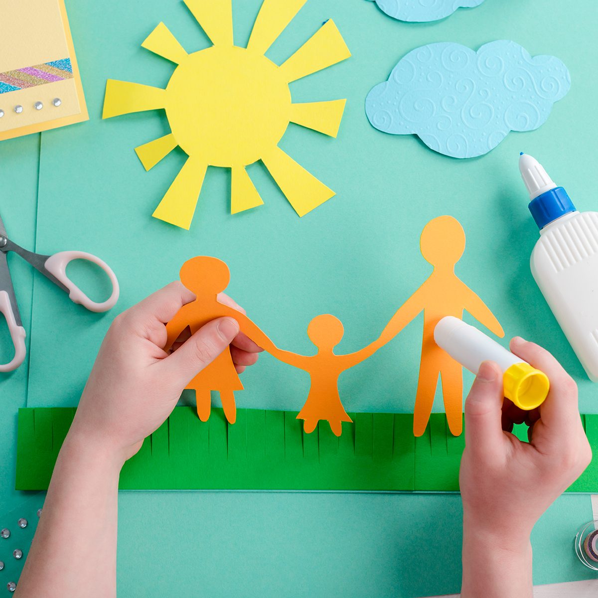 Kid is gluing paper shape on a collage devoted to international family day.
