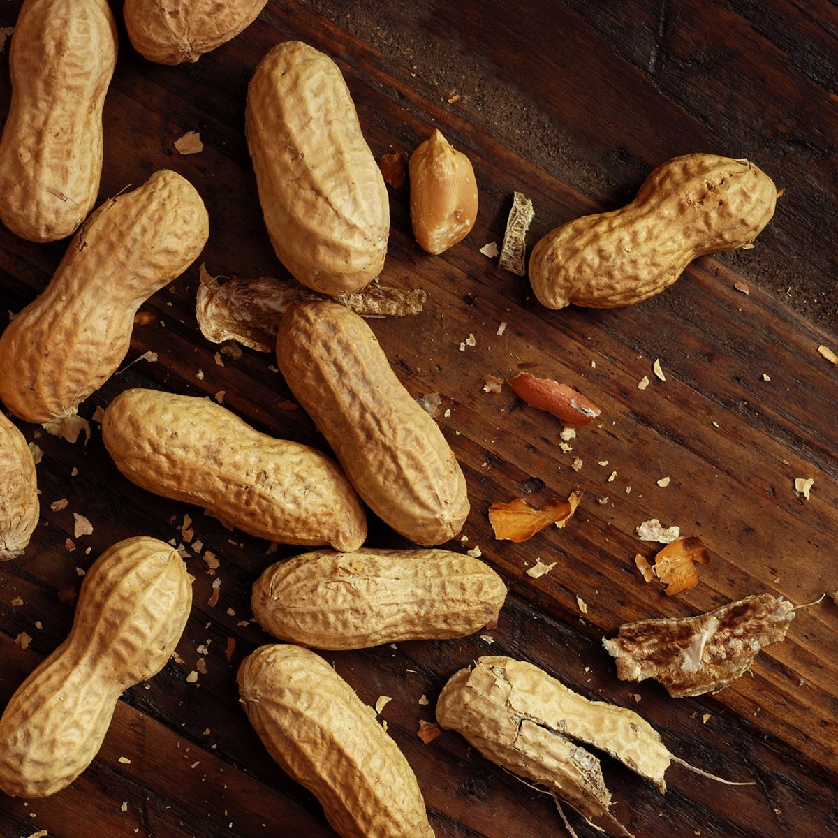 Roasted peanuts with broken shells and pieces scattered on rustic, dark wood background.