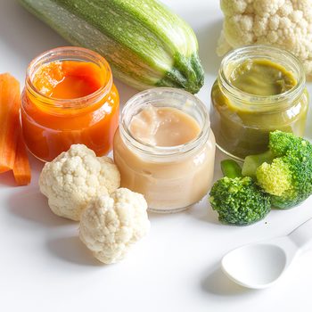 baby mashed with spoon in glass jar on white background